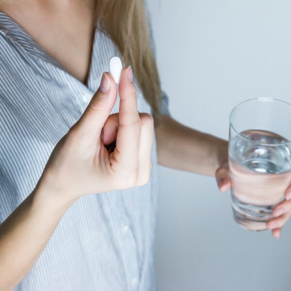 Woman Holding Half-full Glass and White Medicine Pill