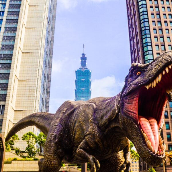 dinosaur with open mouth beside buildings still selective focus photography of